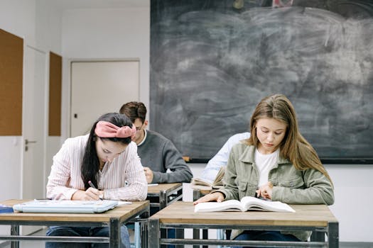 Young students studying in a classroom, focused on reading and writing assignments.